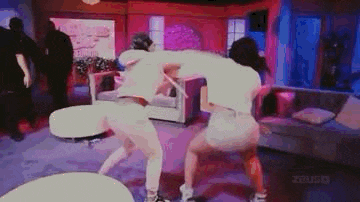 two women are dancing in a living room with a couch and a table .