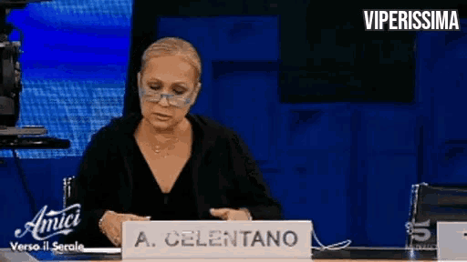 a woman is sitting at a desk with a sign that says a. celentano