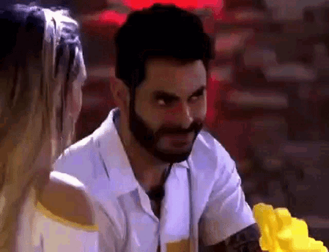 a man with a beard is talking to a woman while holding a yellow flower .