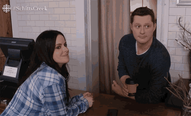 a man and a woman are sitting at a table with #schitts creek written on the bottom
