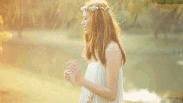 a woman with a flower crown on her head stands in front of a lake