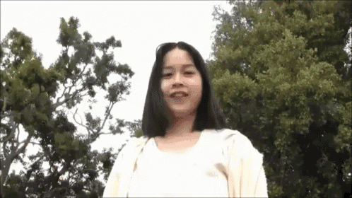 a young woman with long hair is standing in front of trees .