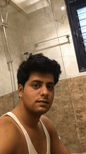 a man in a white tank top is taking a picture of himself in a bathroom