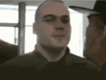 a man in a hat is standing next to another man in a room .