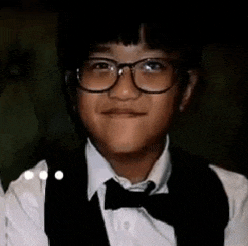 a young boy wearing glasses , a vest and a bow tie is smiling .