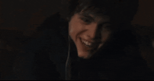 a young boy with curly hair is smiling in the dark
