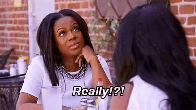 two women are sitting at a table talking to each other and one of them is saying `` really ! ''