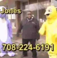 a man in a black jacket is standing next to a purple and yellow stuffed animal .