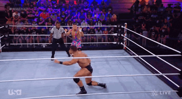 a wrestler is kneeling down in a wrestling ring while a referee looks on .