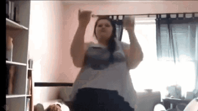 a very fat woman is dancing in a living room with her hands in the air .