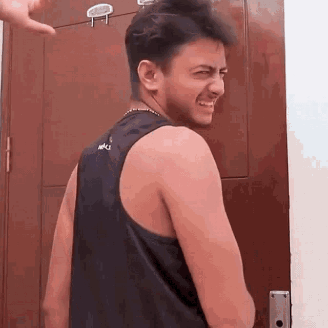 a man wearing a black tank top is standing in front of a door and smiling .