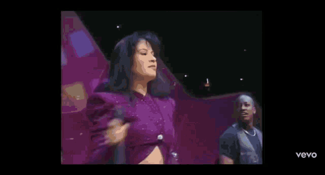 a woman in a purple dress is standing on a stage holding a microphone and dancing .