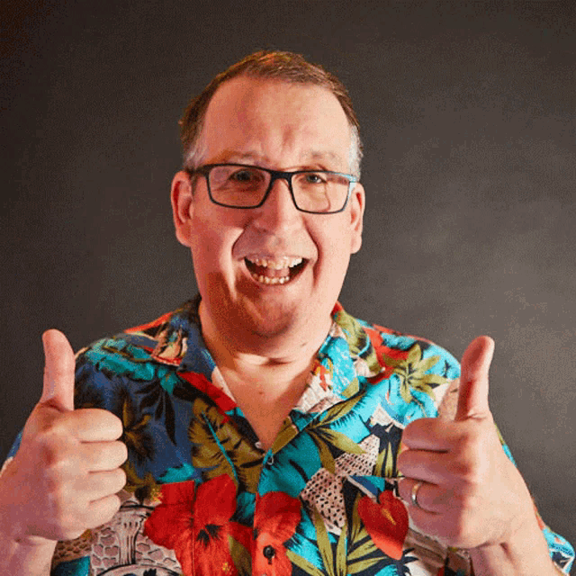 a man wearing glasses and a hawaiian shirt is giving two thumbs up