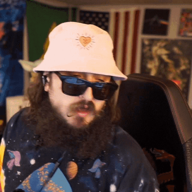 a man with a beard wearing sunglasses and a white hat with a heart on it