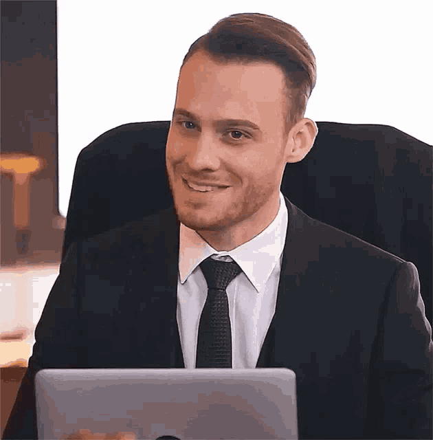 a man in a suit and tie is smiling while using a laptop