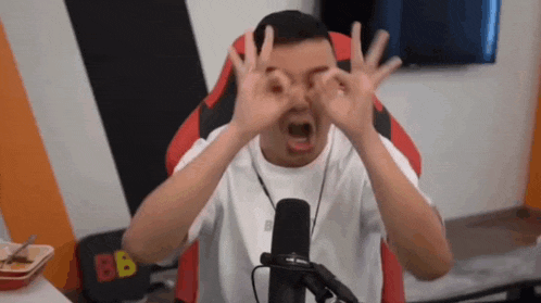 a man is sitting in front of a microphone and making a ok sign with his hands .