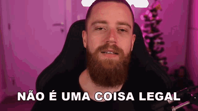 a man with a beard is sitting in front of a microphone with the words " não e uma coisa legal " above him