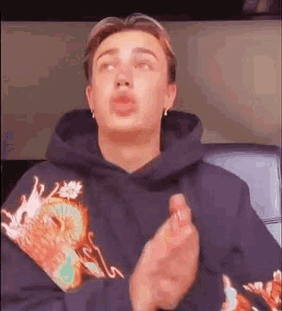 a young man wearing a hoodie is clapping his hands .