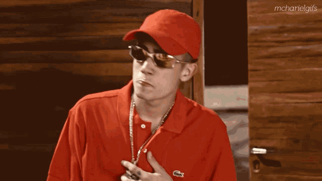 a man wearing a red shirt and a red hat has a necklace around his neck and a tattoo on his arm