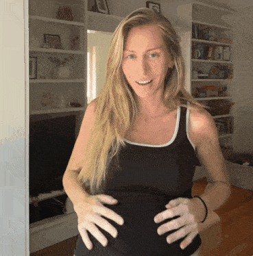 a woman in a black tank top is smiling and holding her belly