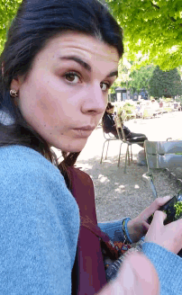 a woman in a blue sweater looks over her shoulder at the camera