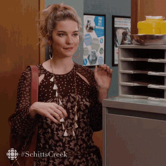 a woman standing in front of a sign that says schittscreek