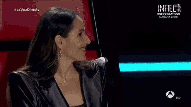 a woman wearing a black leather jacket and earrings is smiling on a tv show .