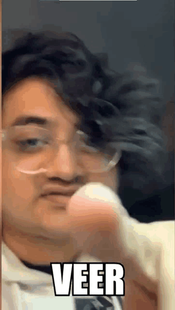 a man wearing glasses is making a funny face and the word veer is on the bottom of his face .