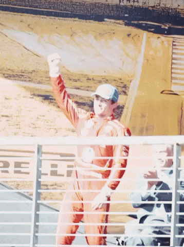 a man in a racing suit holds up his fist in the air