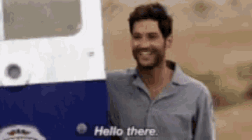 a man with a beard is smiling and standing next to a blue and white vehicle .