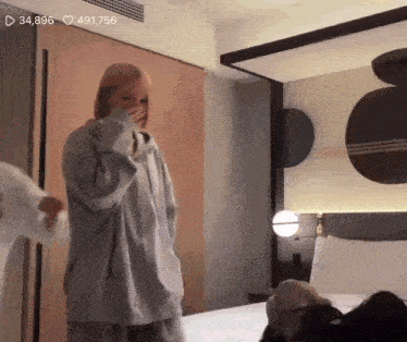 a woman is standing in front of a bed in a hotel room laughing .