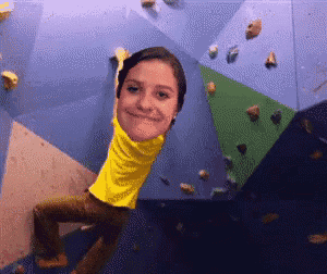 a girl in a yellow shirt is climbing up a wall