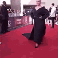 a woman in a long black dress is walking down a red carpet .