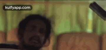 a man with a beard is sitting on a couch while a can is being thrown at him .