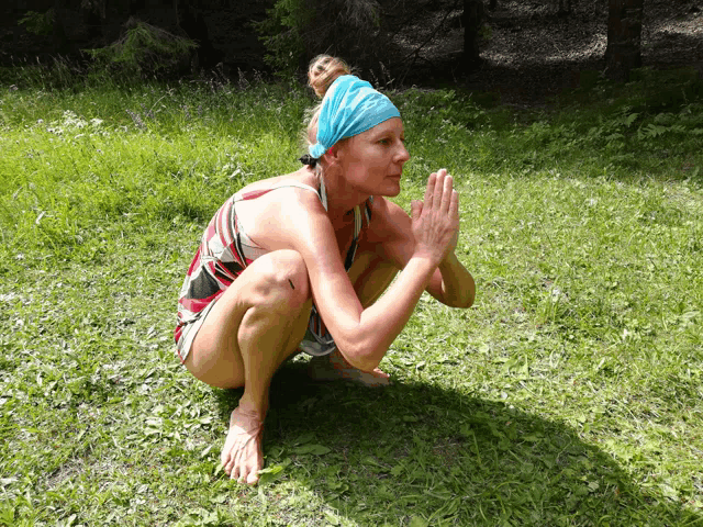 a woman wearing a blue headband is squatting on the grass