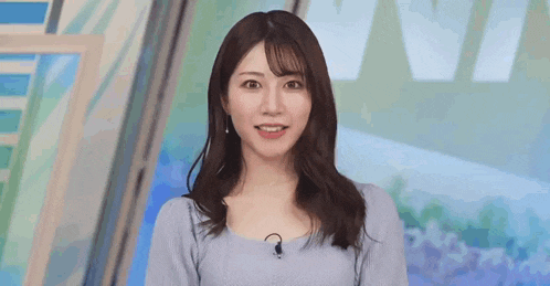 a woman in a blue sweater is standing in front of a microphone and smiling .