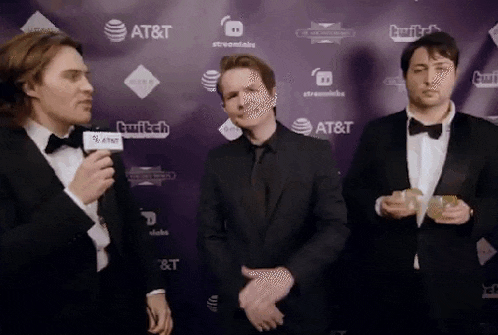 three men in tuxedos and bow ties are standing in front of a purple wall holding trophies .