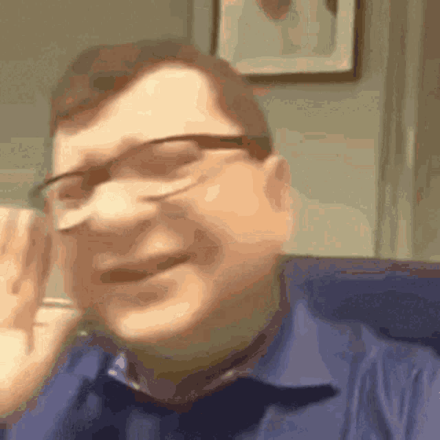 a man wearing glasses and a blue shirt is sitting on a couch and smiling .