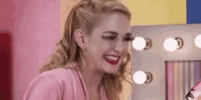 a woman in a pink shirt is smiling in front of a mirror with lights .