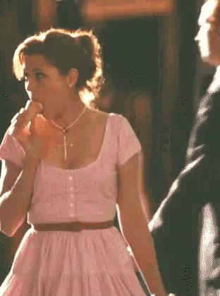 a woman in a pink dress is licking her lips while a man in a suit stands behind her .