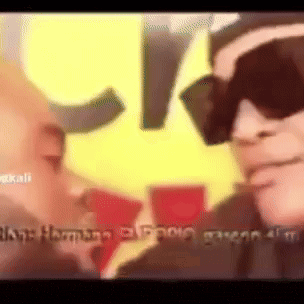 a man wearing sunglasses is talking to another man in front of a yellow and red star .