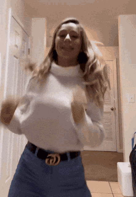 a woman wearing a white sweater and a belt with the letter d on it