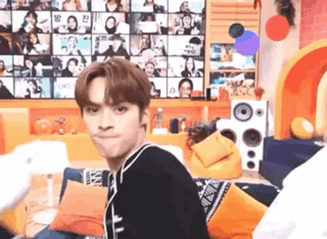 a young man is making a funny face in front of a wall with pictures of people .