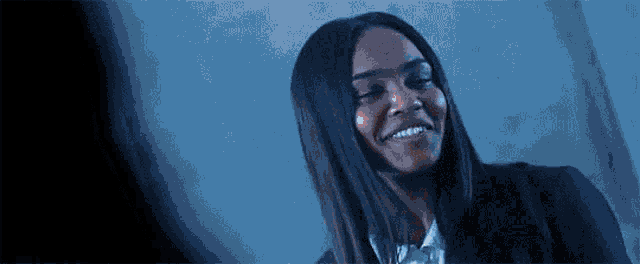 a woman is smiling in a dark room while wearing a suit .