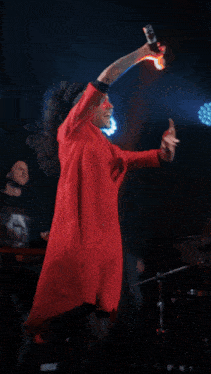 a woman in a red coat is singing into a microphone in front of a sign that says " aci "