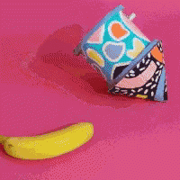 a cup of ice cream with a banana peel sticking out of it on a pink background