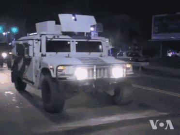 a military vehicle is driving down a street at night with a voa logo in the background