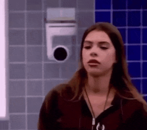a woman is standing in a bathroom with a camera on the wall behind her .