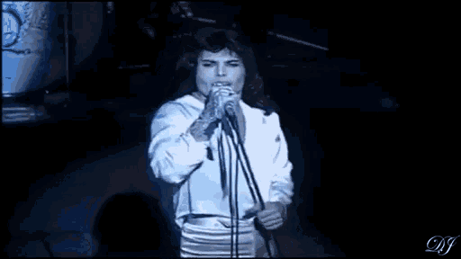 a man in a white shirt is singing into a microphone and giving a middle finger .