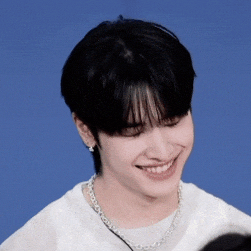 a young man wearing a necklace and earrings smiles